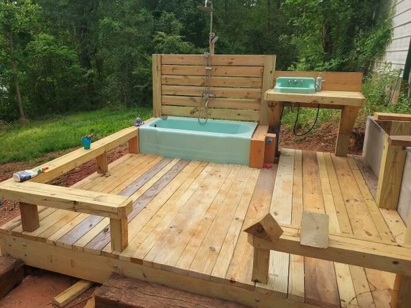 DIY hot tub with wooden deck, makeshift fence, and a small sink in a backyard.
