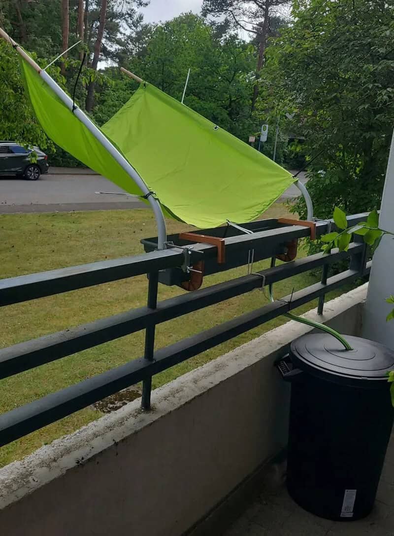 A makeshift sunshade with a green fabric and metal poles on a balcony.