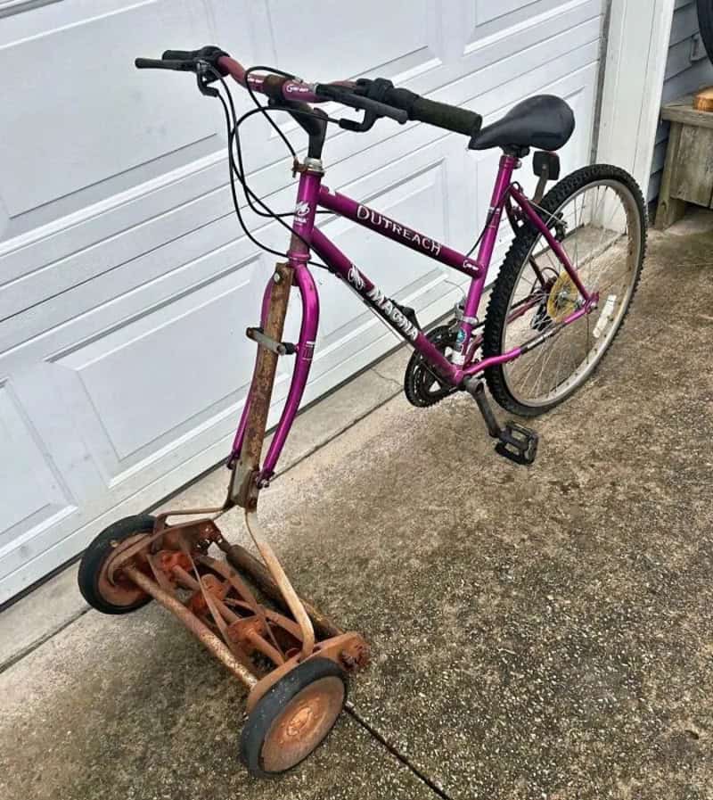 Rusty lawnmower attached to a pink bicycle, creating a makeshift vehicle.