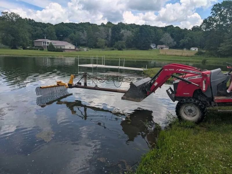 Red tractor with a makeshift boat propeller on a lake.