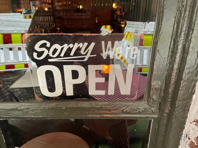 Sorry We're OPEN sign in a window with construction in background.