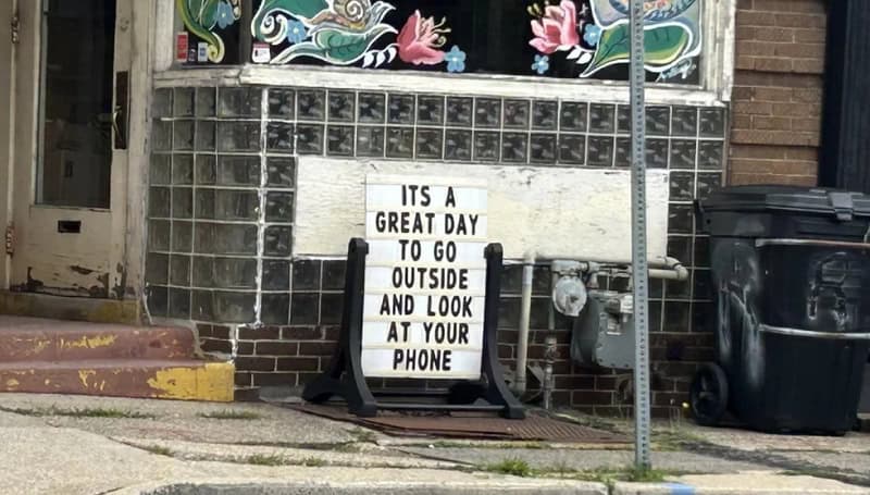Sign says 'It's a great day to go outside and look at your phone'.