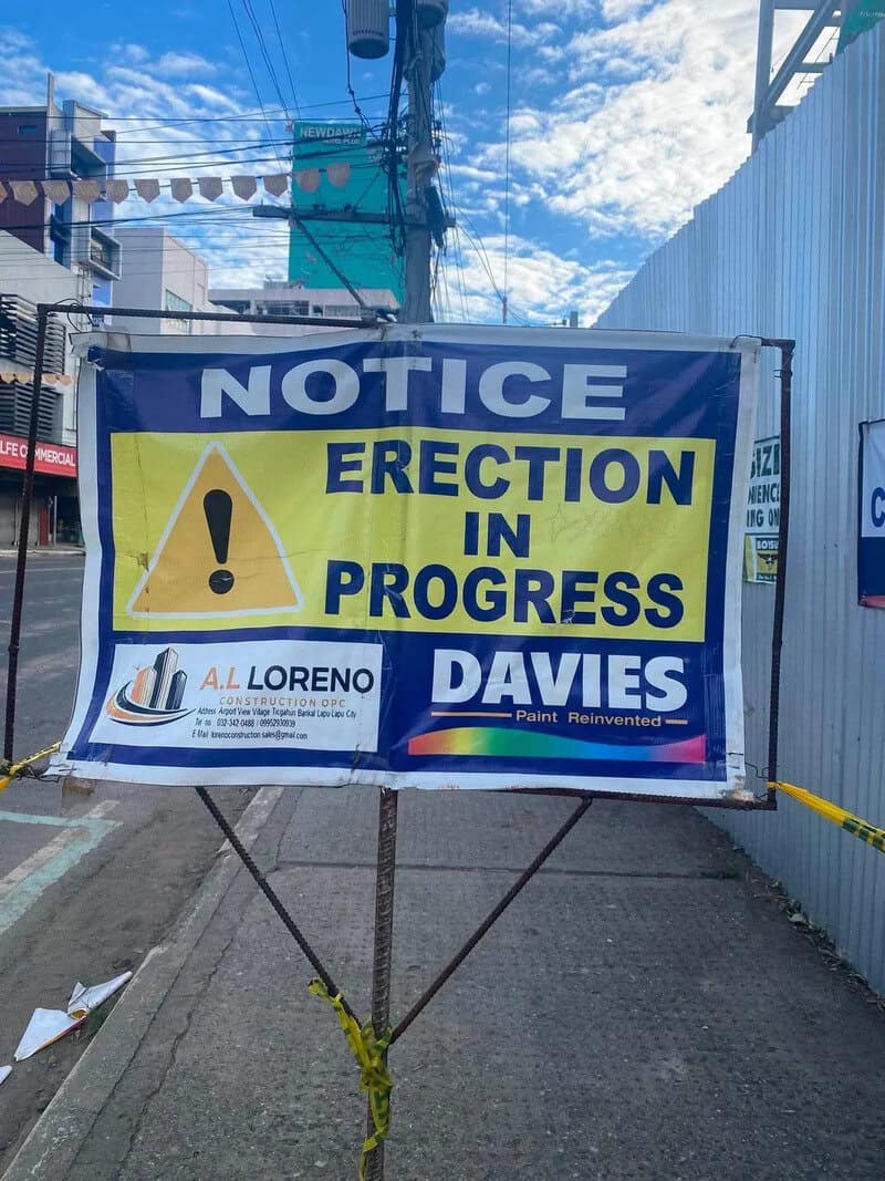 Notice sign saying 'Erection in Progress' with construction logos and rainbow colors.