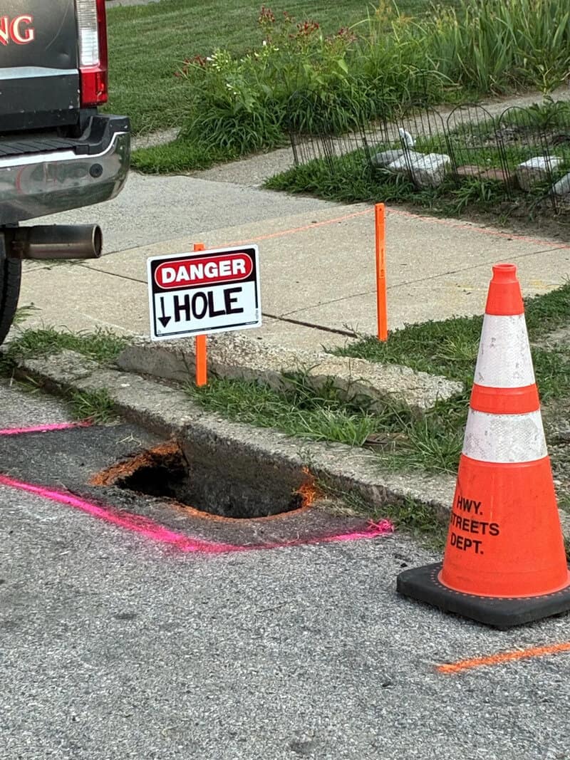 Warning sign says 'DANGER HOLE' near an open hole in the street.