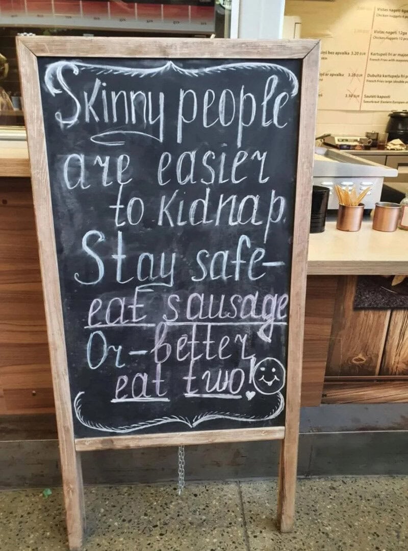 Chalkboard sign with humorous message about skinny people and eating sausage.