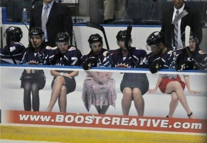 Hockey players sitting on the bench with a woman in a pink dress among them.