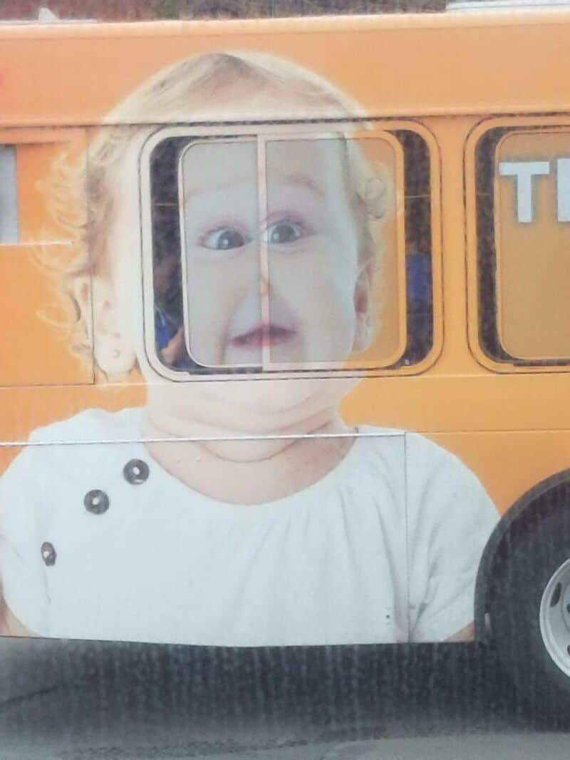 Child looking out of a bus window with a surprised expression.