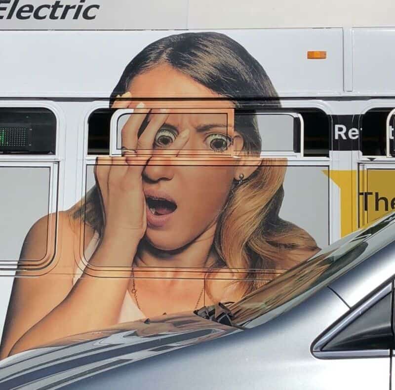 Woman with surprised expression on a bus with a large advertisement.