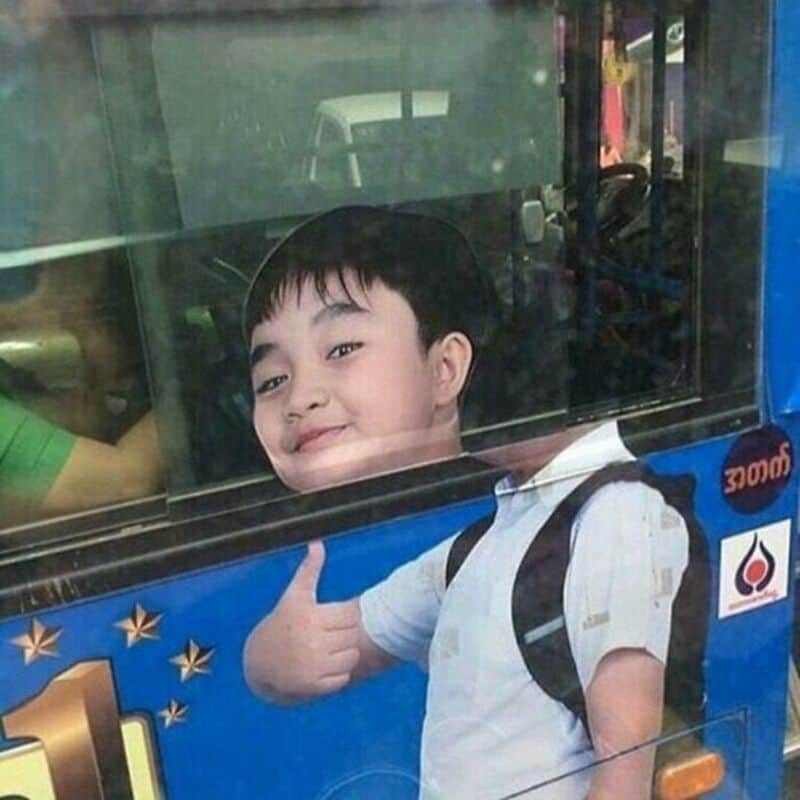 Young boy giving a thumbs-up through a bus window.