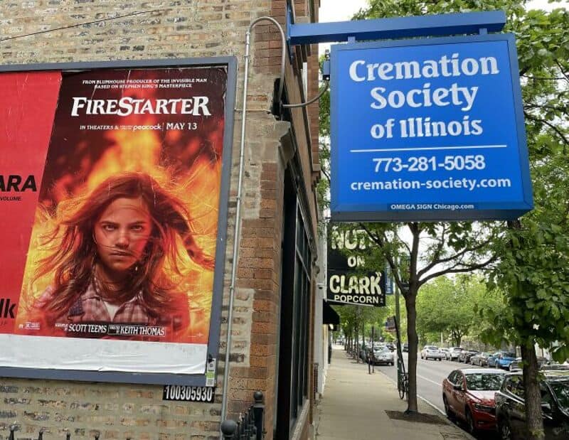 Cremation Society of Illinois sign and Firestarter movie poster on a city sidewalk.