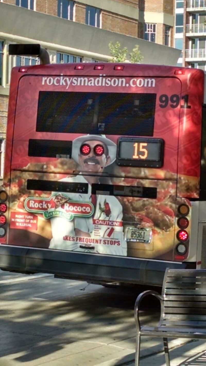 Back of a red bus with a robot face and advertising, route 15, 99.1, in Madison.