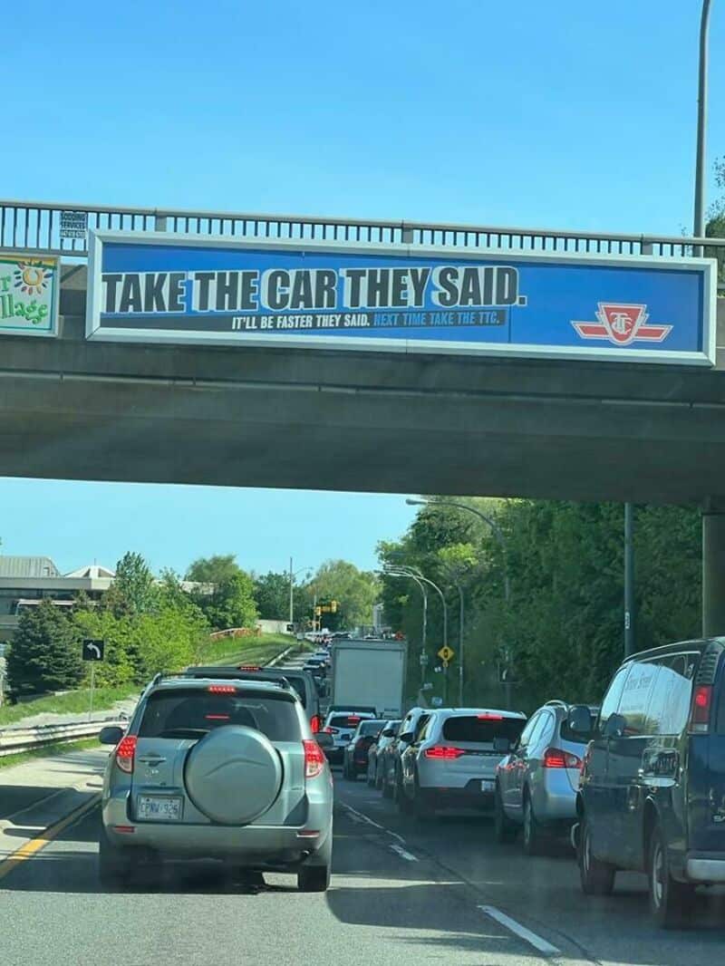 Billboard on overpass reads 'TAKE THE CAR THEY SAID. IT'LL BE FASTER THEY SAID. JUST TRY TAKE THE T1.