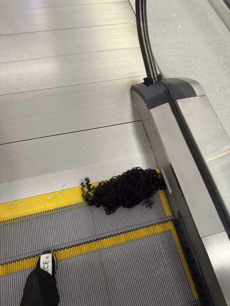 Curly black hair on an airport moving walkway with a shoe in the corner.