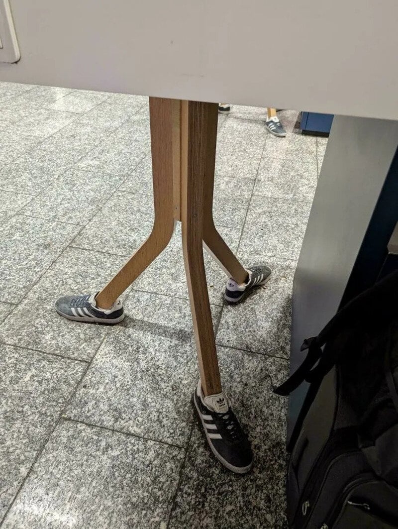 Person with legs and sneakers seen through a gap in a table at an airport.