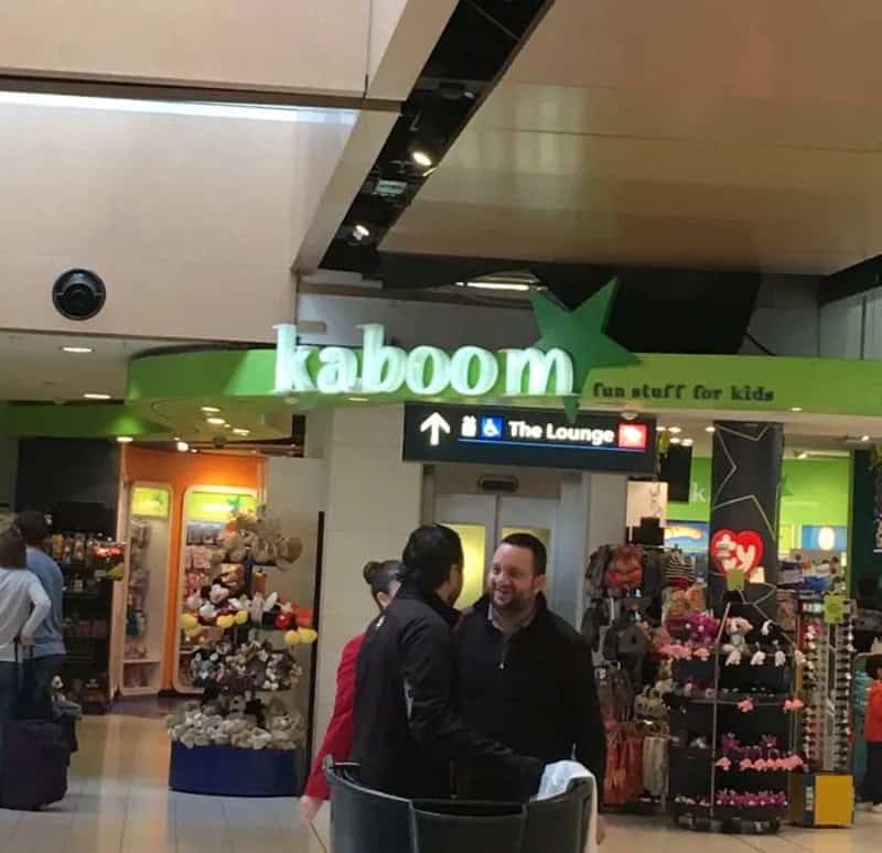 People talking near Kaboom store at airport with sign for The Lounge.