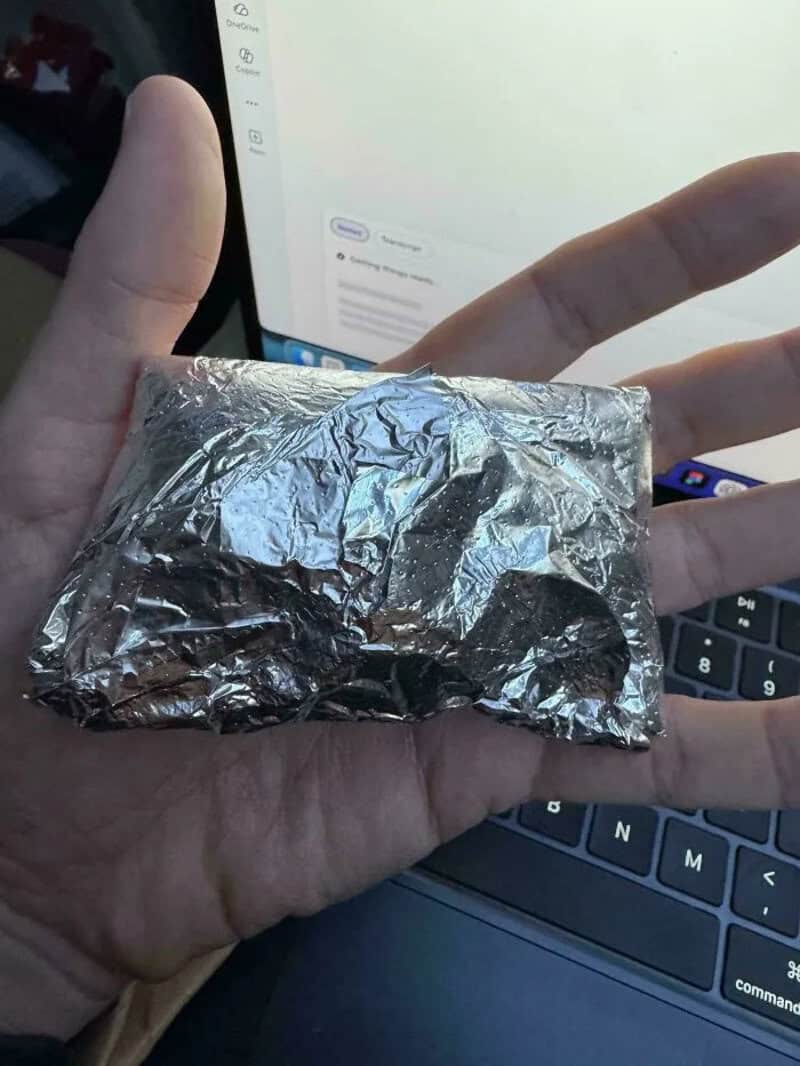 Person holding a small foil-wrapped package in front of a laptop.