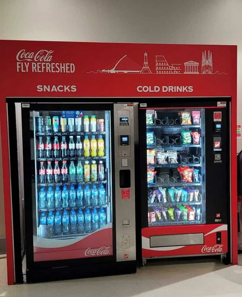 Vending machines with snacks and cold drinks at an airport.