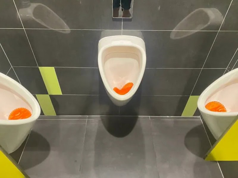 Urinals with orange soap or sponge inside, in a men's restroom.