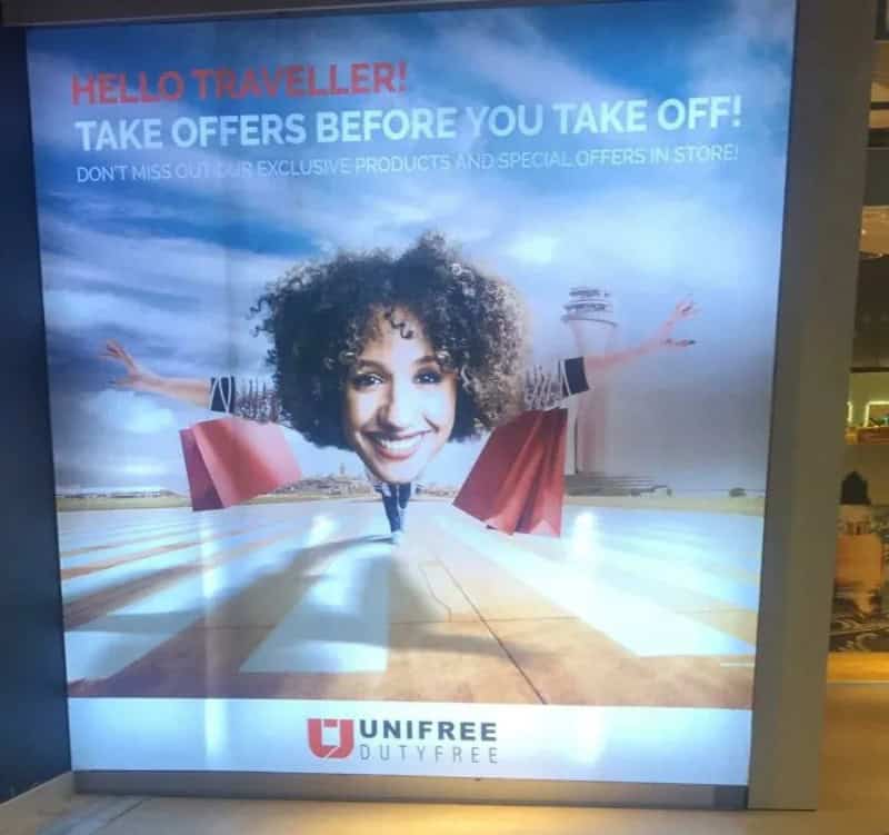Travel advertisement with a woman with curly hair holding shopping bags at an airport.