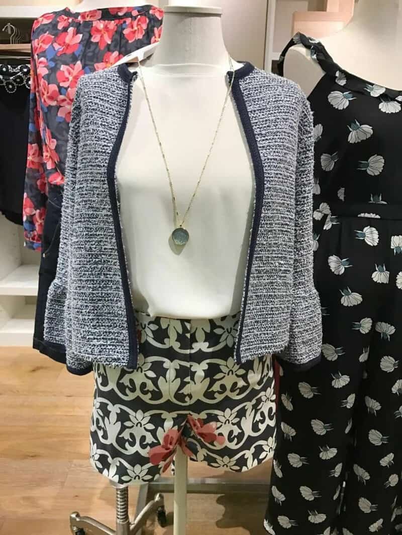 Mannequin wearing a grey jacket, white top, and patterned shorts with a pink bow.