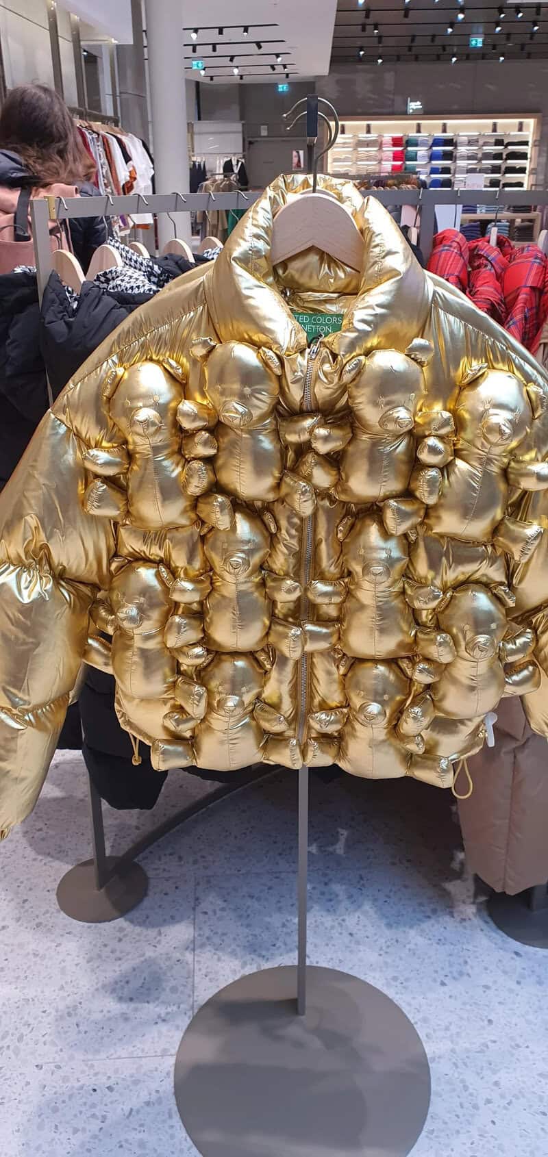 Gold puffer jacket with numerous small teddy bear figures attached.