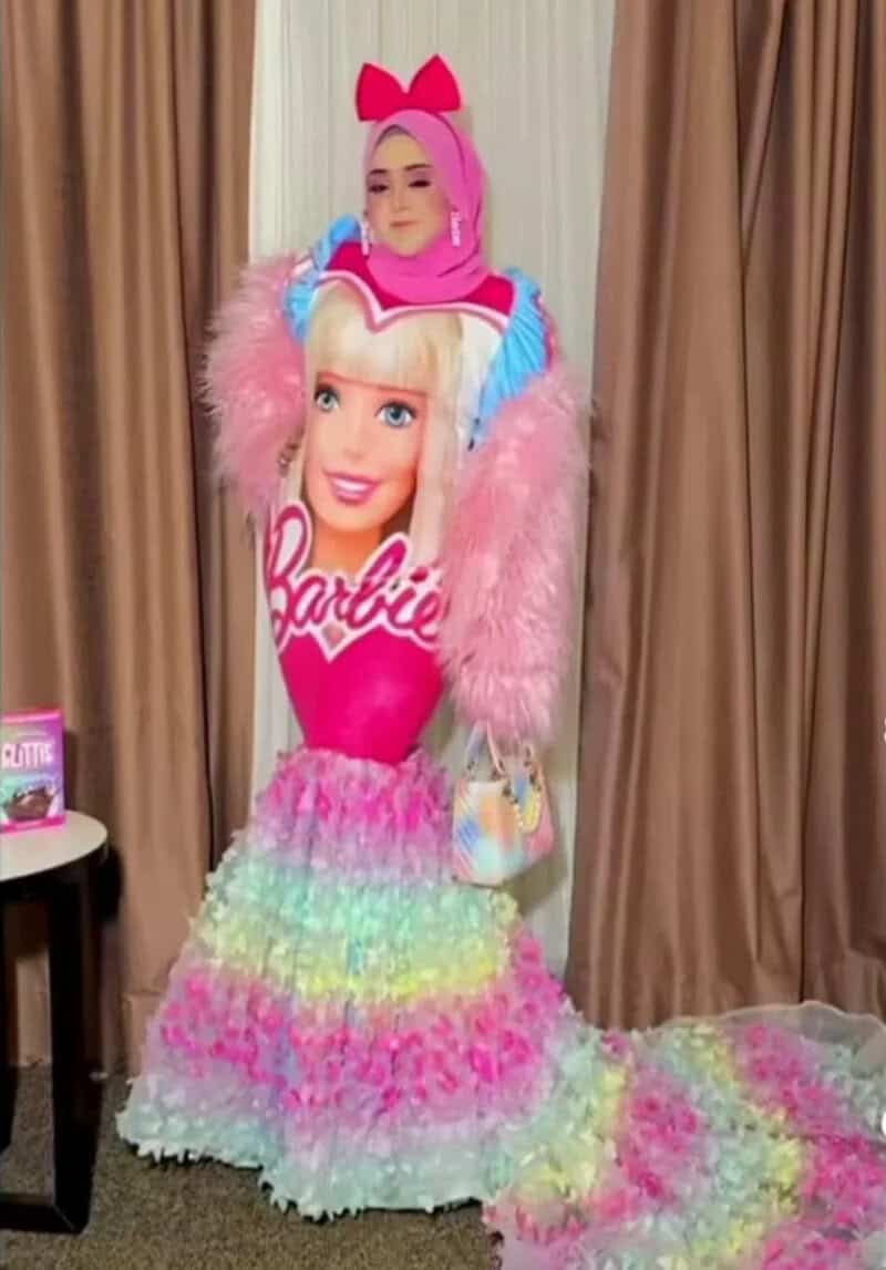 Woman dressed as Barbie with pink wig, rainbow skirt, and pink bow headband.