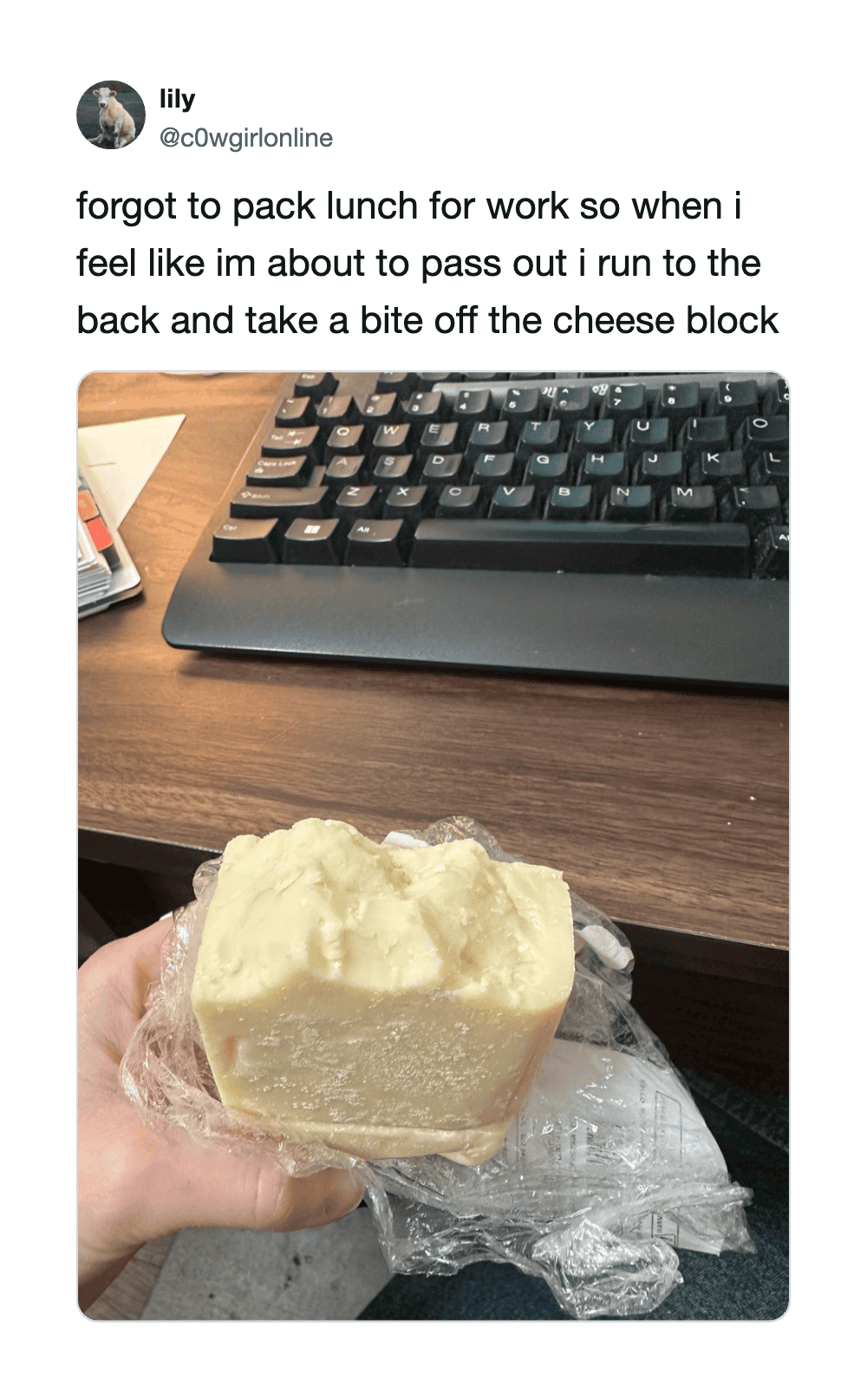 Hand holding a piece of cheese in front of a keyboard on a desk.
