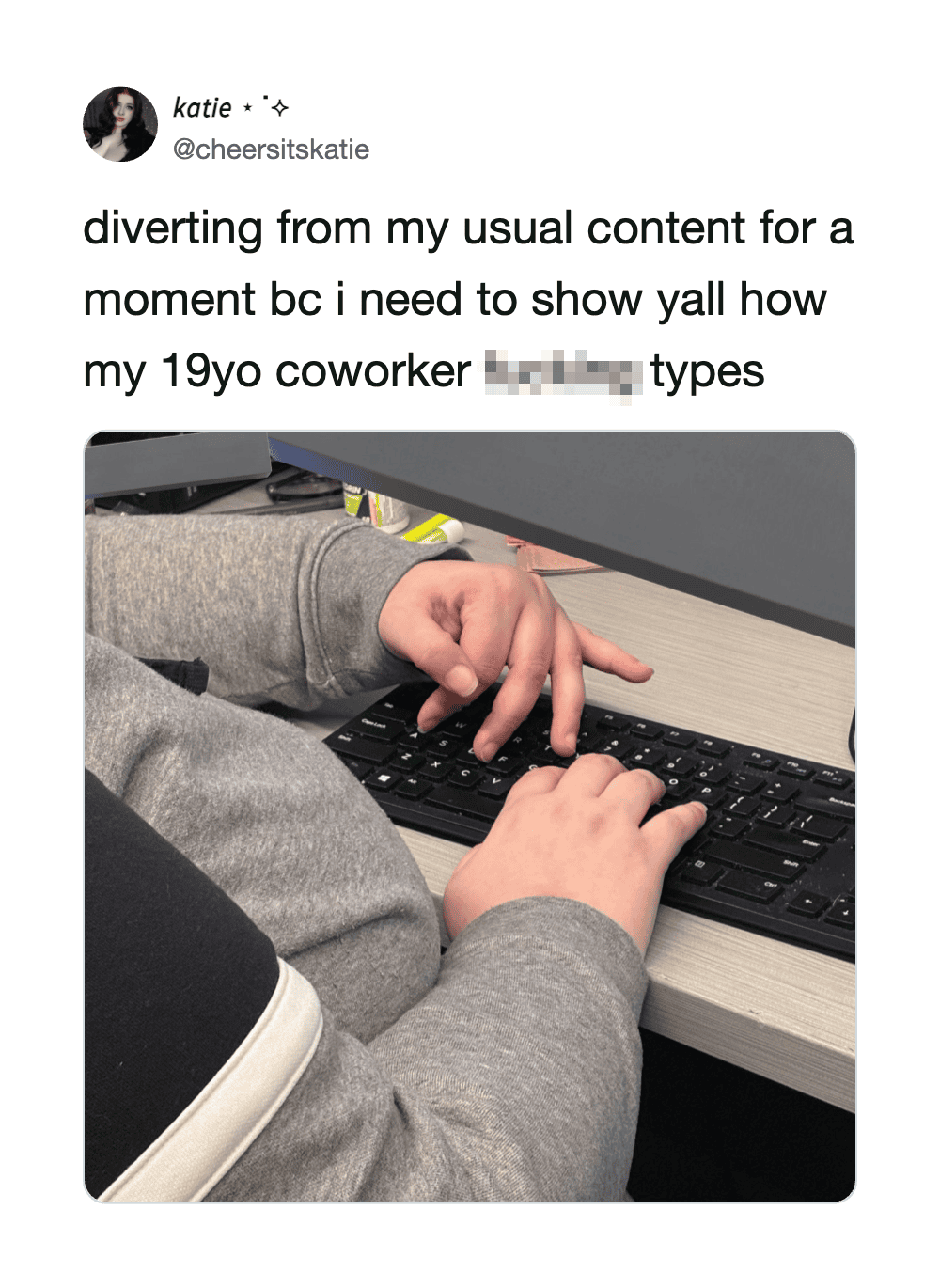 Young coworker typing on a keyboard at a desk, wearing a gray hoodie.