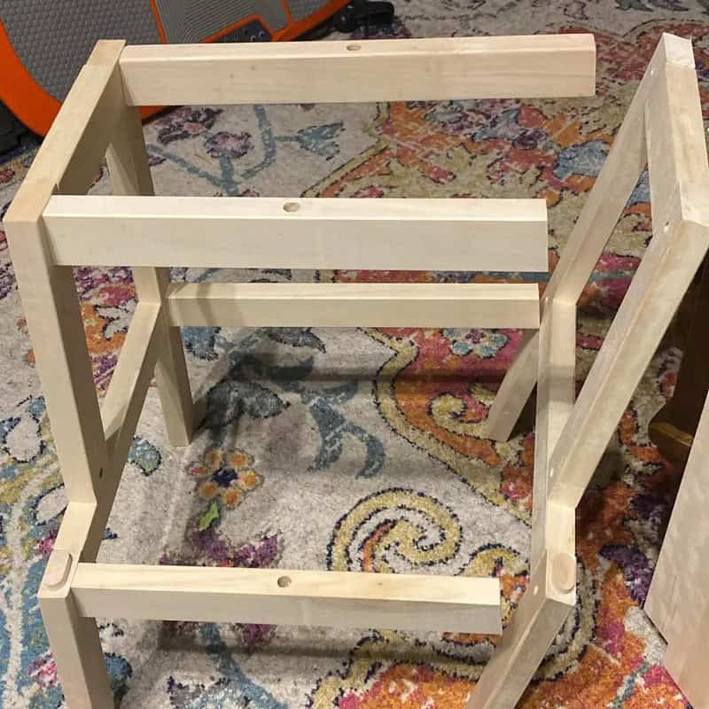 Unassembled wooden furniture frame on a colorful rug.