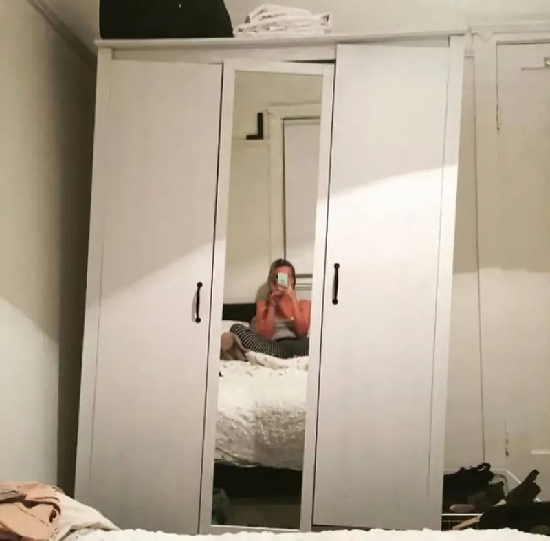 White wardrobe with a mirror door reflecting a person taking a photo.