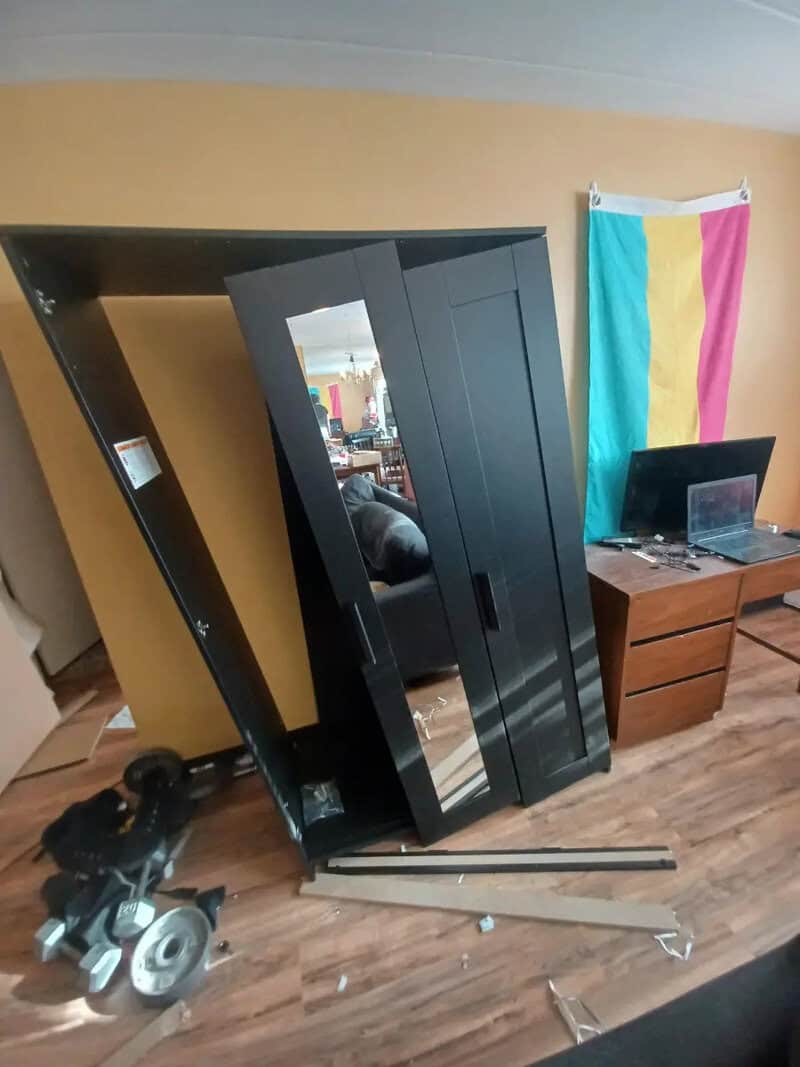 Black wardrobe tilted with fallen support on a wooden floor.