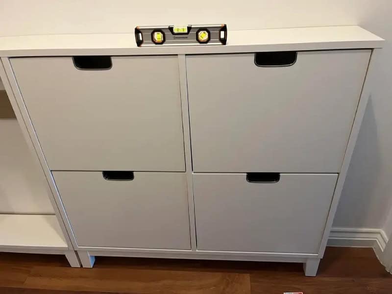 Level placed on top of a white cabinet with four drawers, furniture assembly fail.