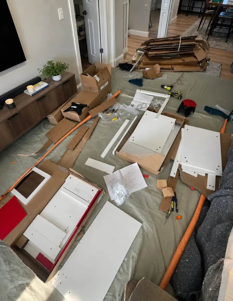Disorganized living room with furniture parts, tools, and packaging scattered around.