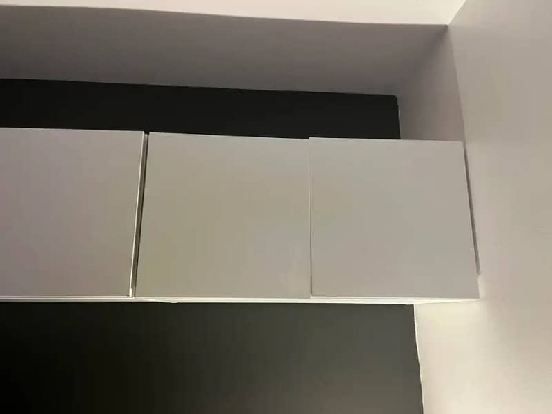 Three white cabinets mounted on a wall with a black background above.