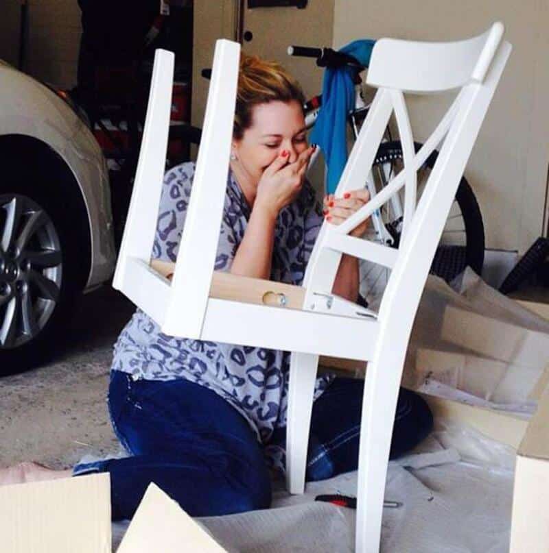 Woman laughing with a chair in a garage, furniture assembly fail.