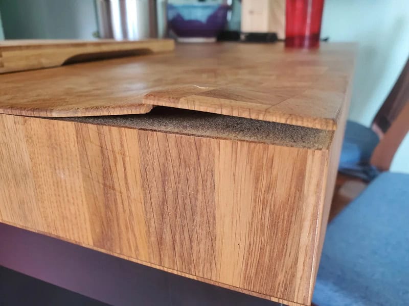 Broken wooden table edge with a large chip and crack.