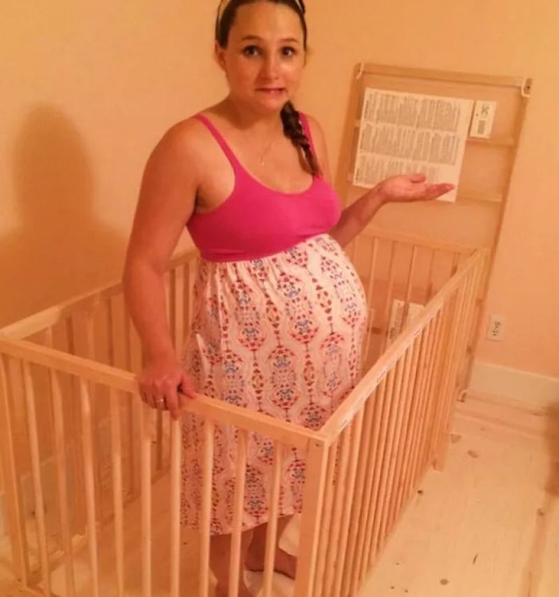 Woman in a pink top and patterned skirt inside a wooden crib, holding a manual.