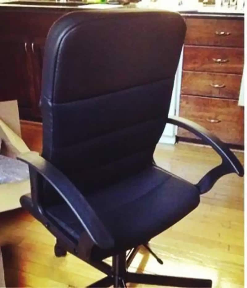 Black office chair with broken armrest in a room with wooden furniture.