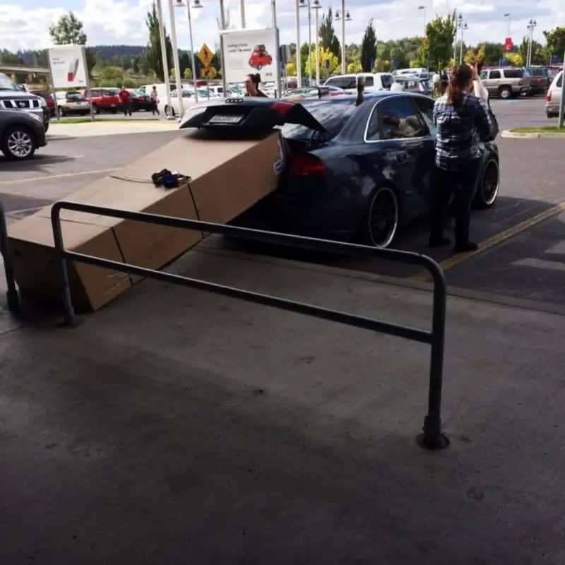 Car with large cardboard box on trunk, blocking rear view, in parking lot.