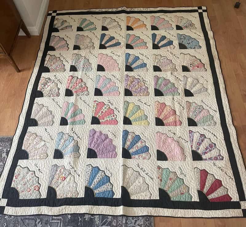 Colorful quilt with fan patterns and black borders on a wooden floor.