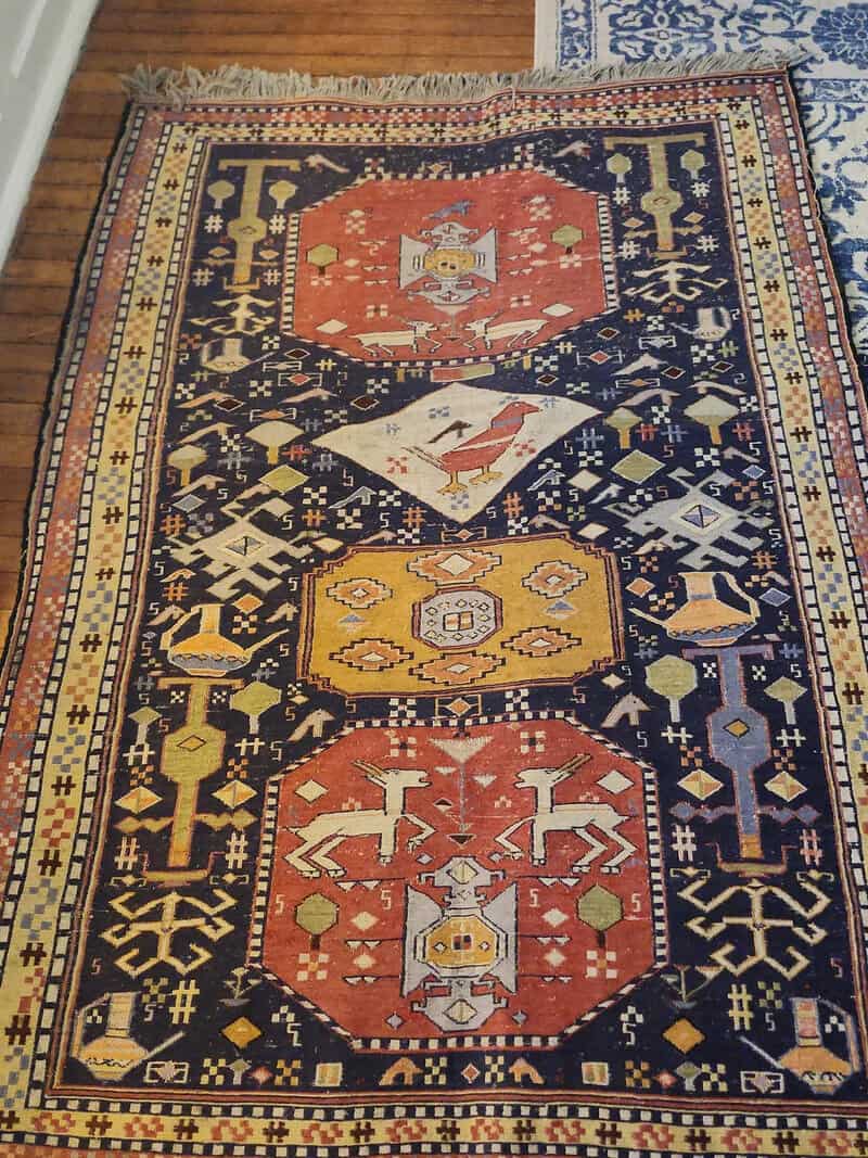 Colorful rug with geometric and animal patterns, including deer and birds.