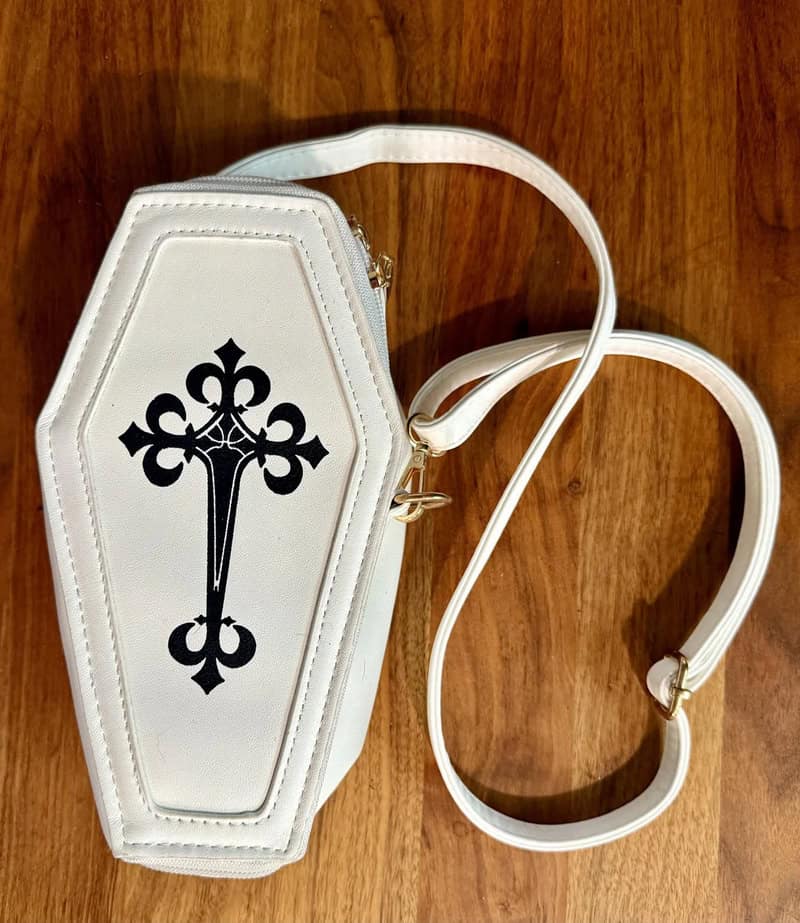White handbag with black cross design and detachable strap on wooden surface.