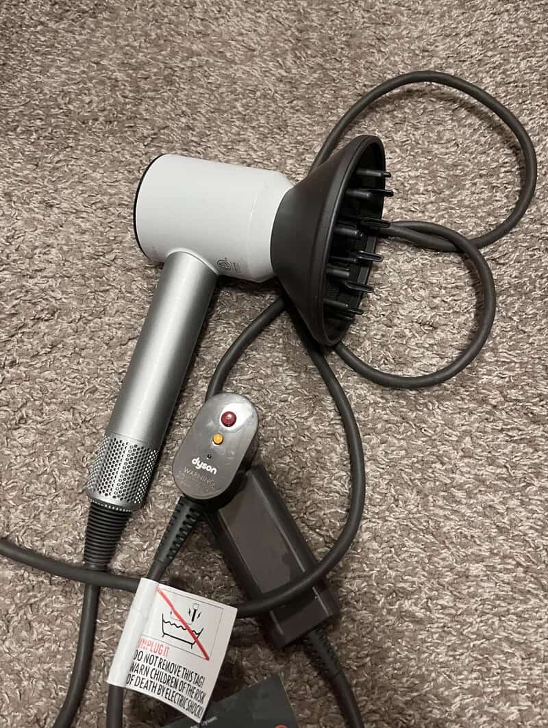 A Dyson hair dryer with a diffuser attachment on a carpeted floor.