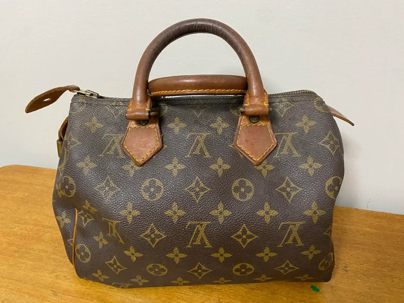 Louis Vuitton handbag with monogram pattern and leather handles on a wooden surface.