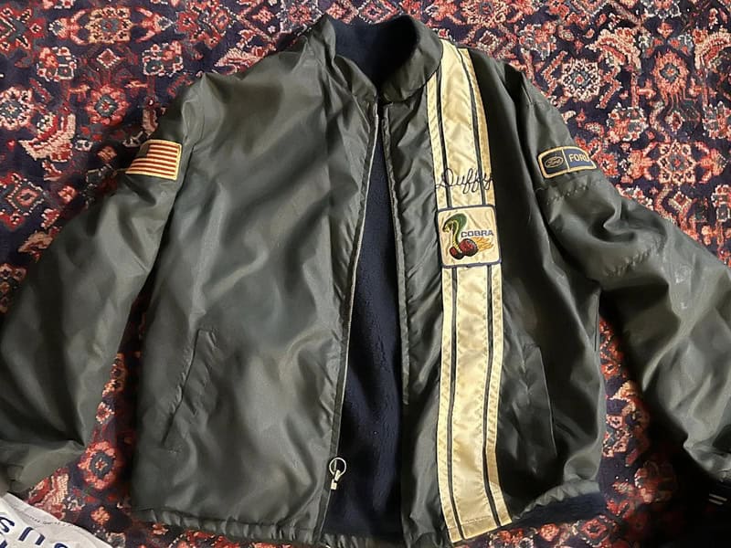 Vintage bomber jacket with patches and stripes, laid on a patterned rug.
