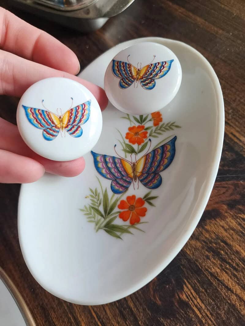 Two white ceramic salt and pepper shakers with colorful butterfly designs on a floral dish.
