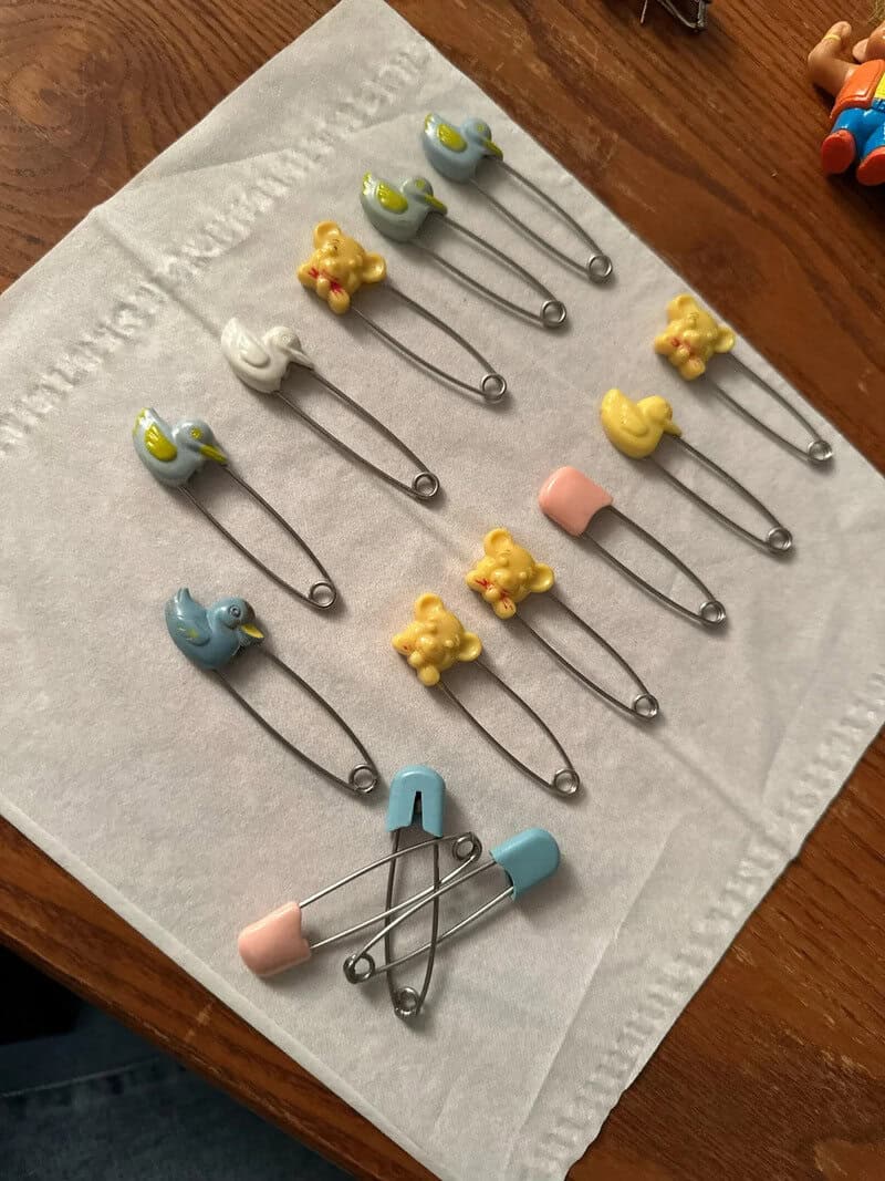Assorted baby safety pins with animal and duck designs on a white cloth.