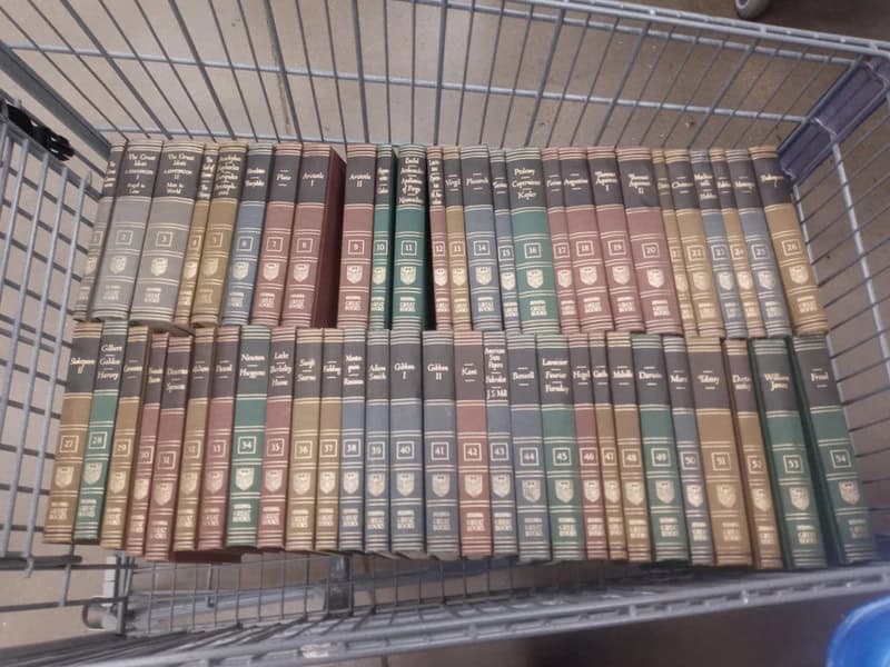 A shopping cart filled with old, colorful hardcover books with gold and silver embossing.