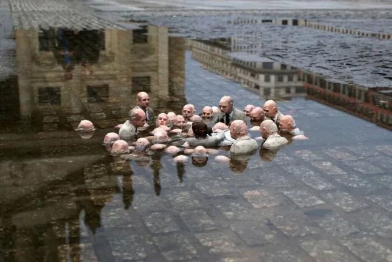 Group of small figurines with bald heads in a pool of water on a city street.