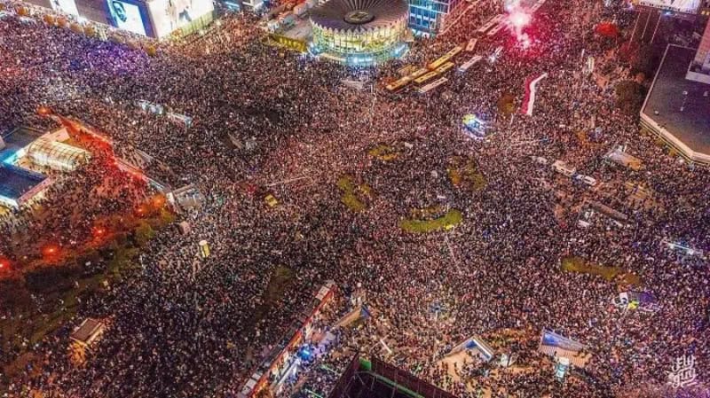 Aerial view of a large crowd gathered in a city square at night.